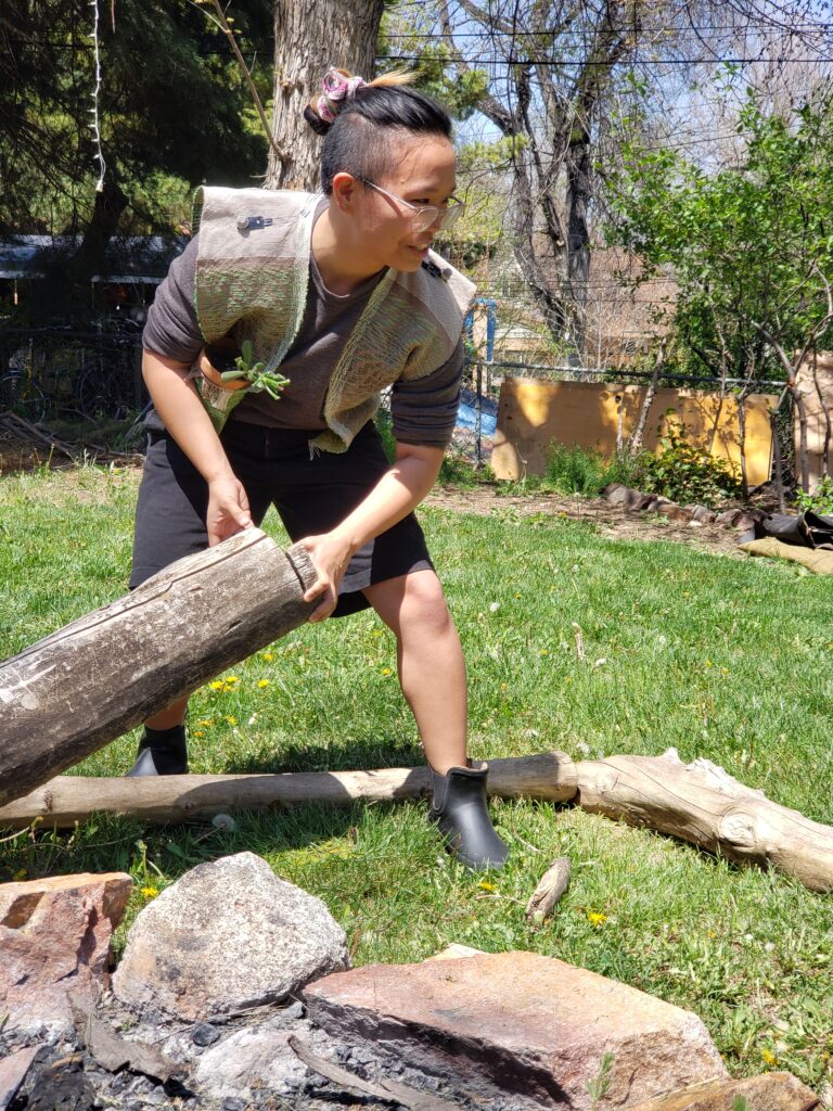 Shanel wears the Ozone Vest while lifting a log in their backyard.